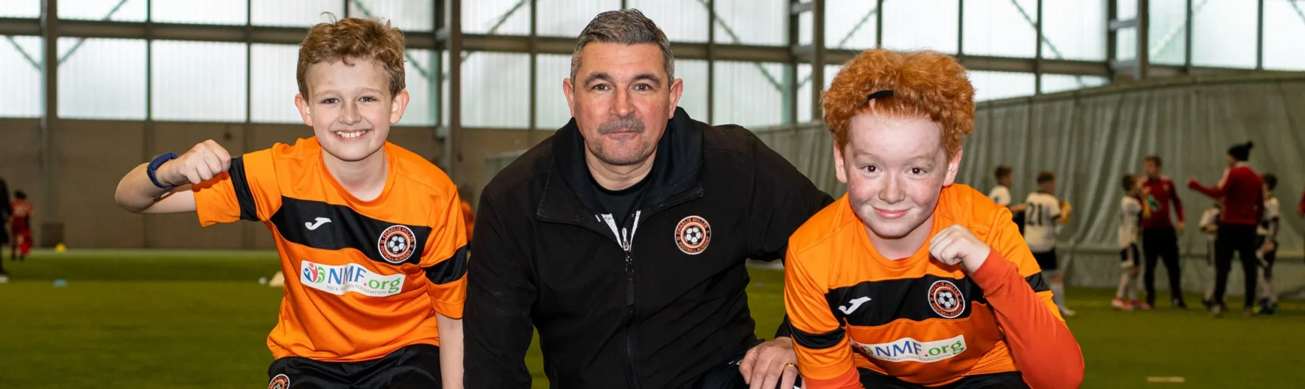 Charlie Miller with two young players of his academy, in the academy kit with the NMF badge